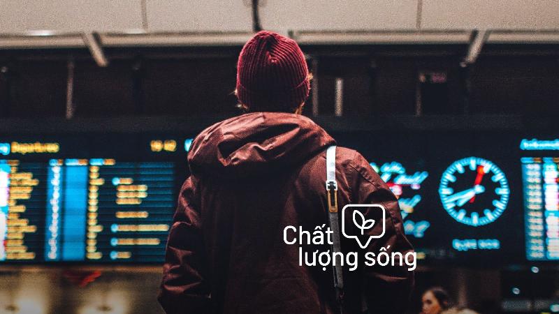 Một hành khách nữ đang ngồi thoải mái tại cửa ra tàu bay, kiểm tra thông tin trên điện thoại với vẻ bình tĩnh, hành lý gọn gàng bên cạnh, thể hiện sự chuẩn bị kỹ lưỡng và chuyến đi suôn sẻ.